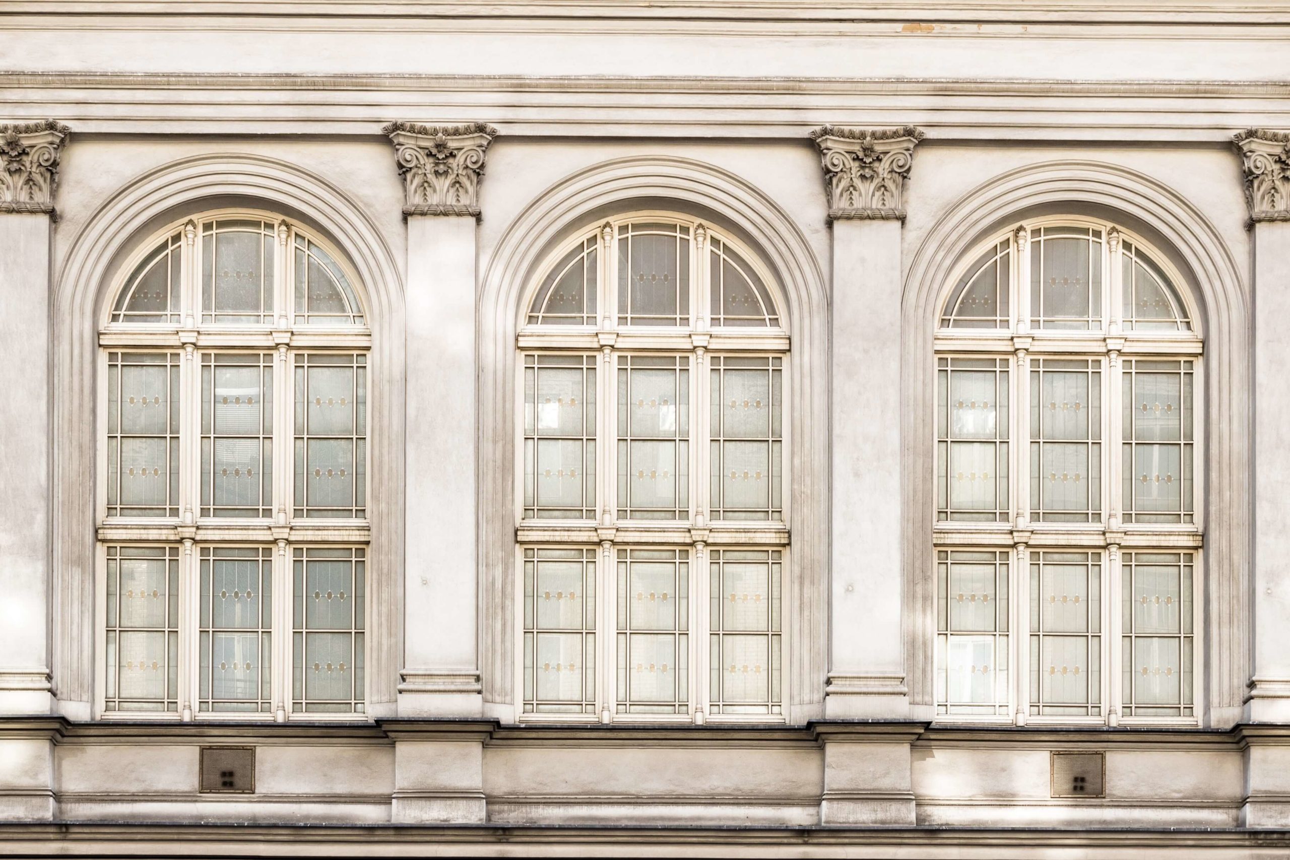 Three large, arched windows with ornate decorative columns between them are set in a white facade. The windows have a grid pattern, adding a symmetrical touch to the buildings exterior.